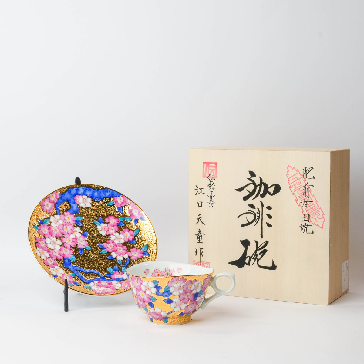 Close-up of the ornate cherry blossom decorated tea cup with gold trim, showing pink, white, and blue floral patterns on a white background