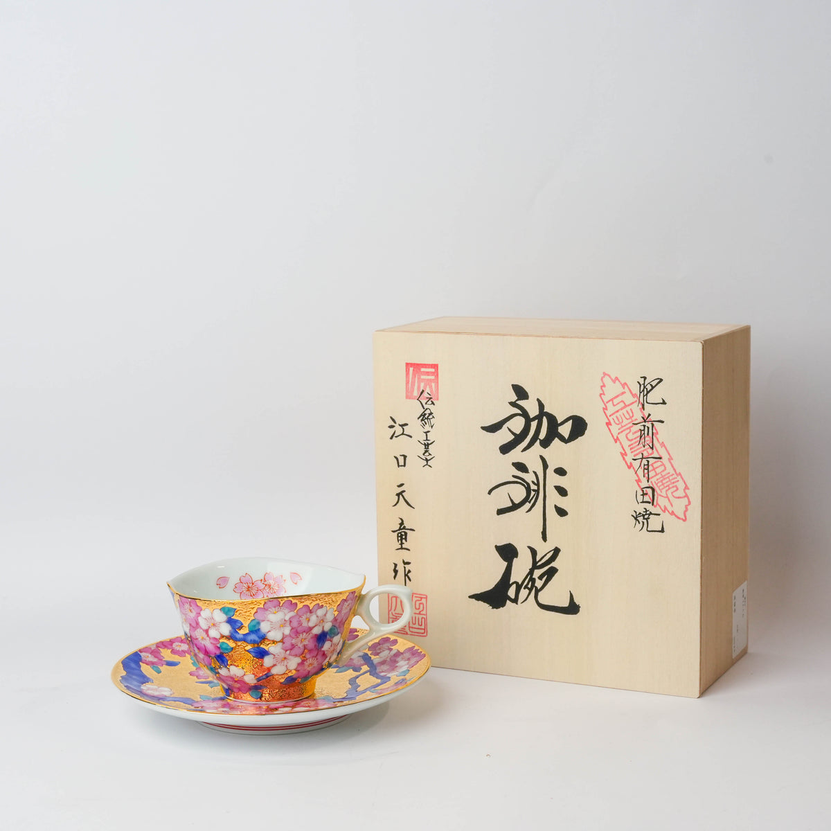 Colorful Japanese porcelain tea cup with pink cherry blossom floral design, gold accents, and a white handle, on a white background