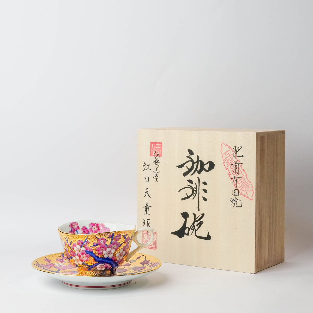 Colorful Japanese porcelain teacup with plum blossom design, gold accents, and a matching saucer, part of a traditional tea set.