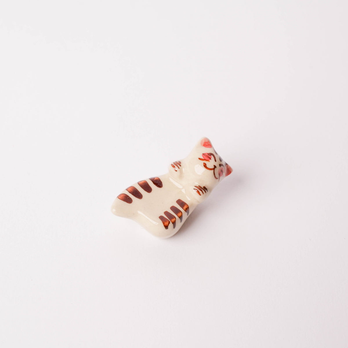 Hand-painted ceramic cat chopstick rest with orange and brown stripes, playful feline design, on white background