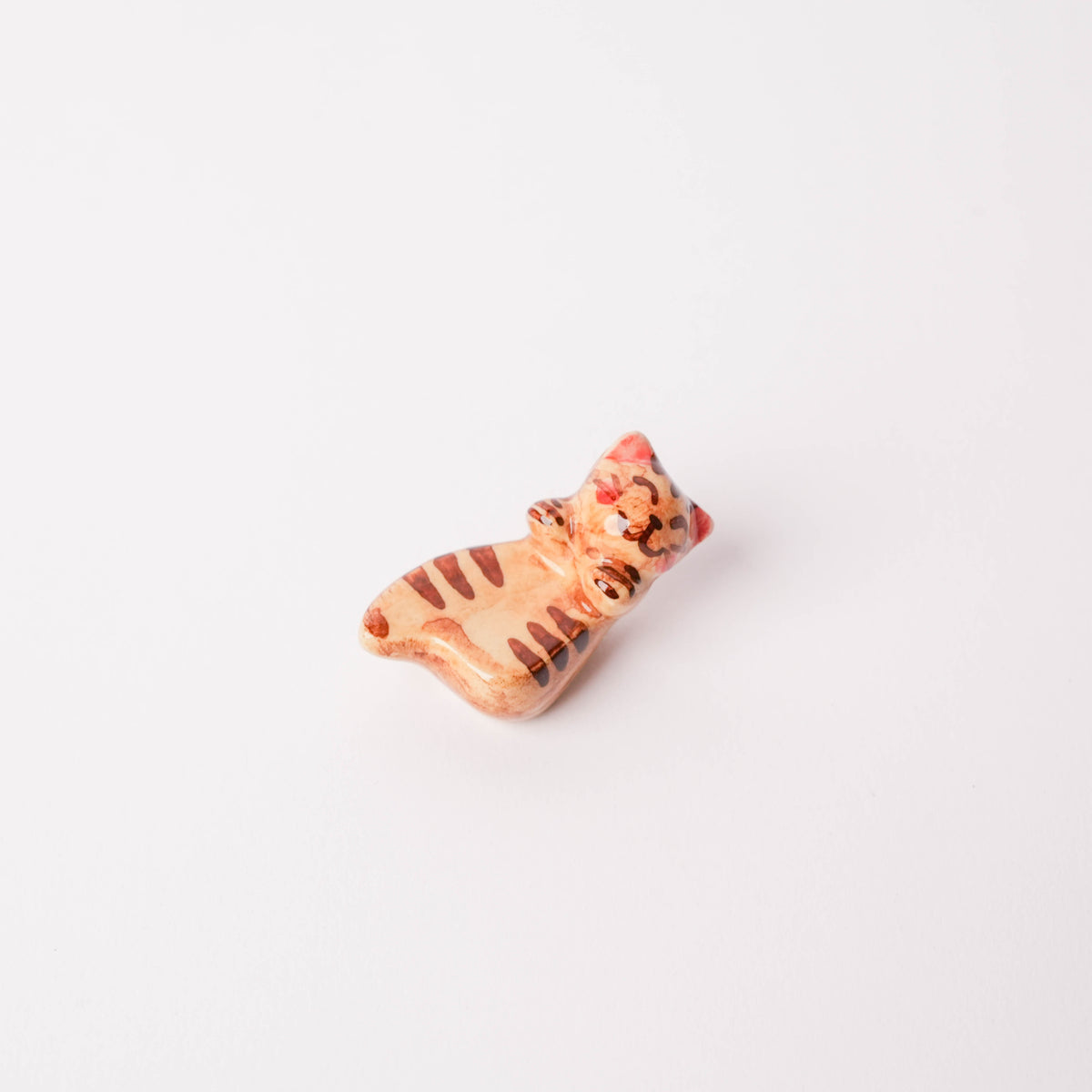 Close-up of ceramic cat chopstick rest with orange and brown striped pattern, detailed feline face, on white surface