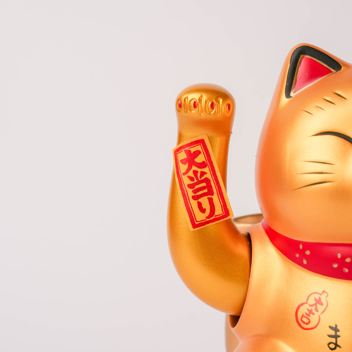Close-up of the gold Lucky Cat's face with a smiling expression, red and black accents, and detailed Japanese inscriptions