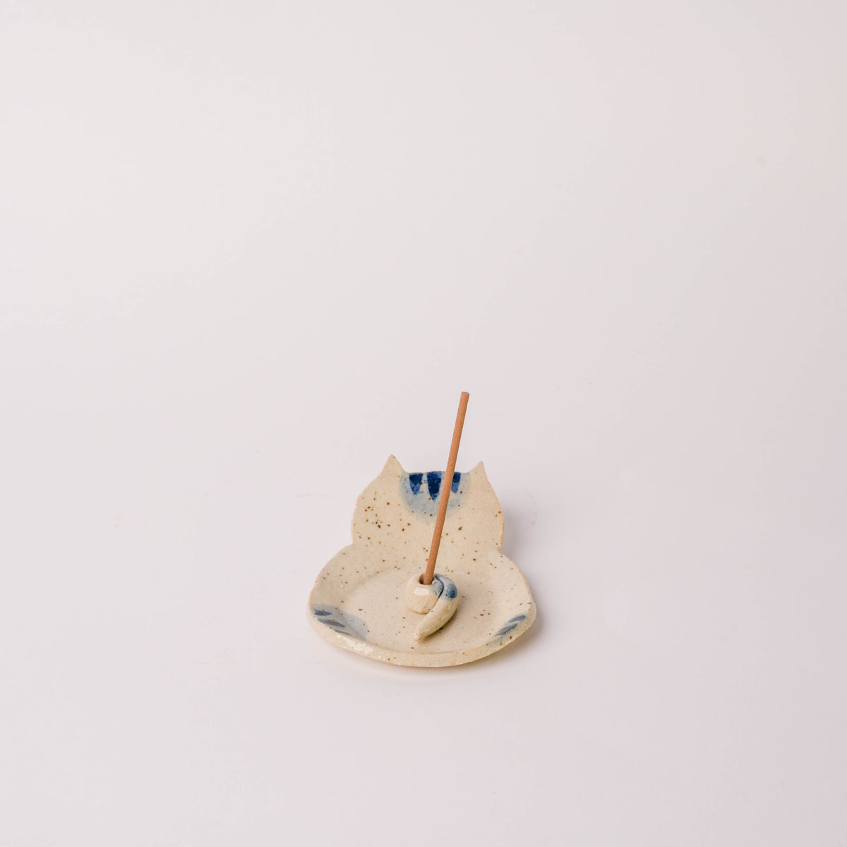 Ceramic curled tail cat incense holder in beige with blue accents, featuring a playful cat design, holds incense sticks and catches ash.