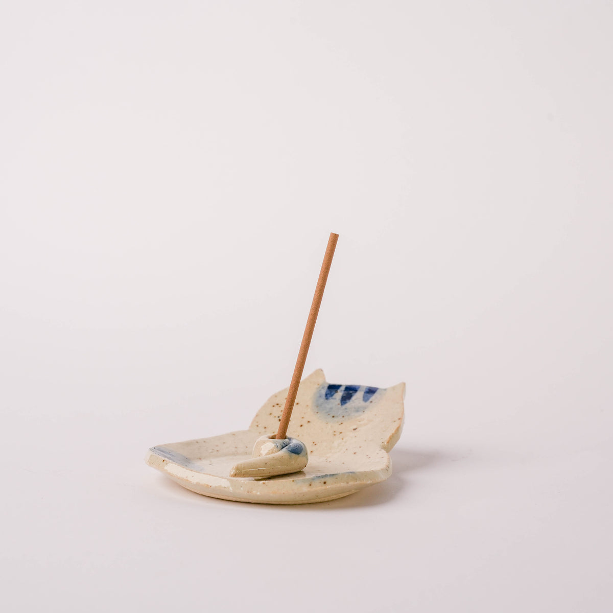 Ceramic cat incense holder with a base, beige with blue accents, featuring a playful cat design, on a white background.