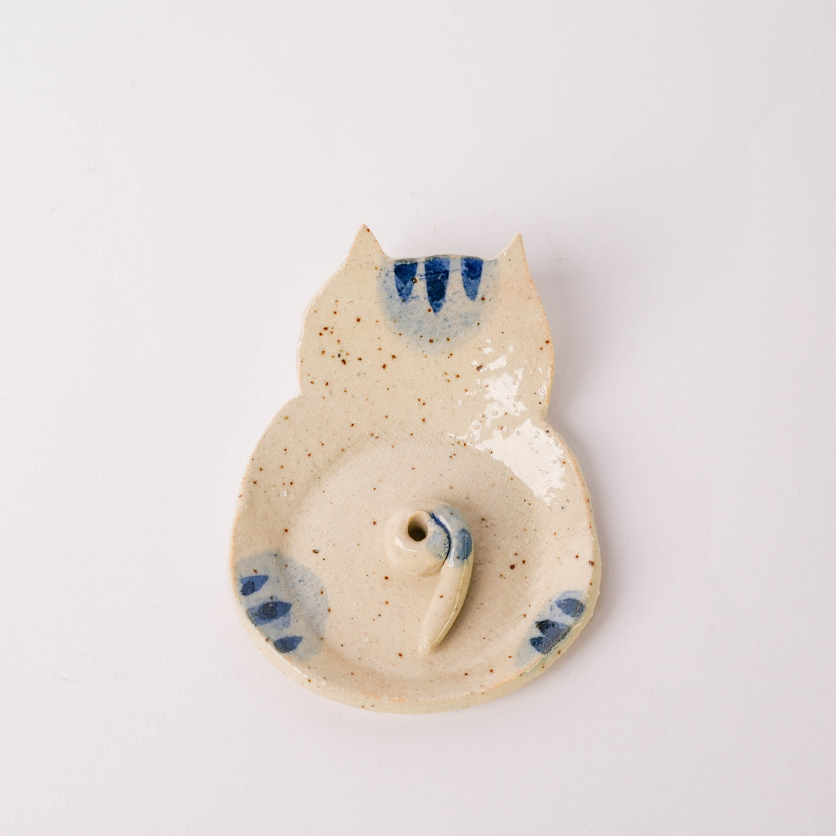 Close-up of ceramic cat incense holder with a curled tail, beige with blue decorative accents, on a white background.