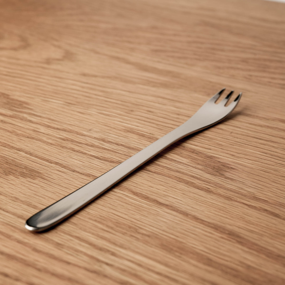 Stainless steel dessert fork with three tines, weighted handle, on a wooden surface, part of the Sori Yanagi Hime Fork collection.