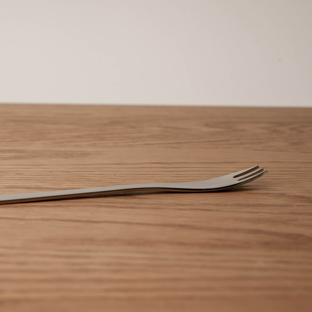 Plain wooden surface with a white background, showcasing the minimalist design of the stainless steel dessert fork.