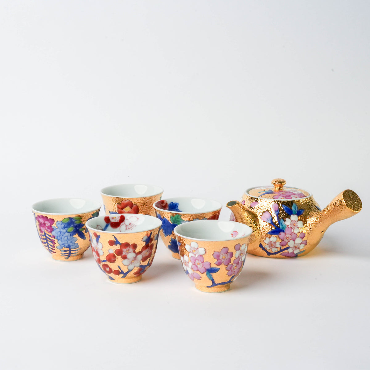 Close-up of a gold teapot with pink cherry blossom and blue floral designs, detailed craftsmanship for traditional tea serving.