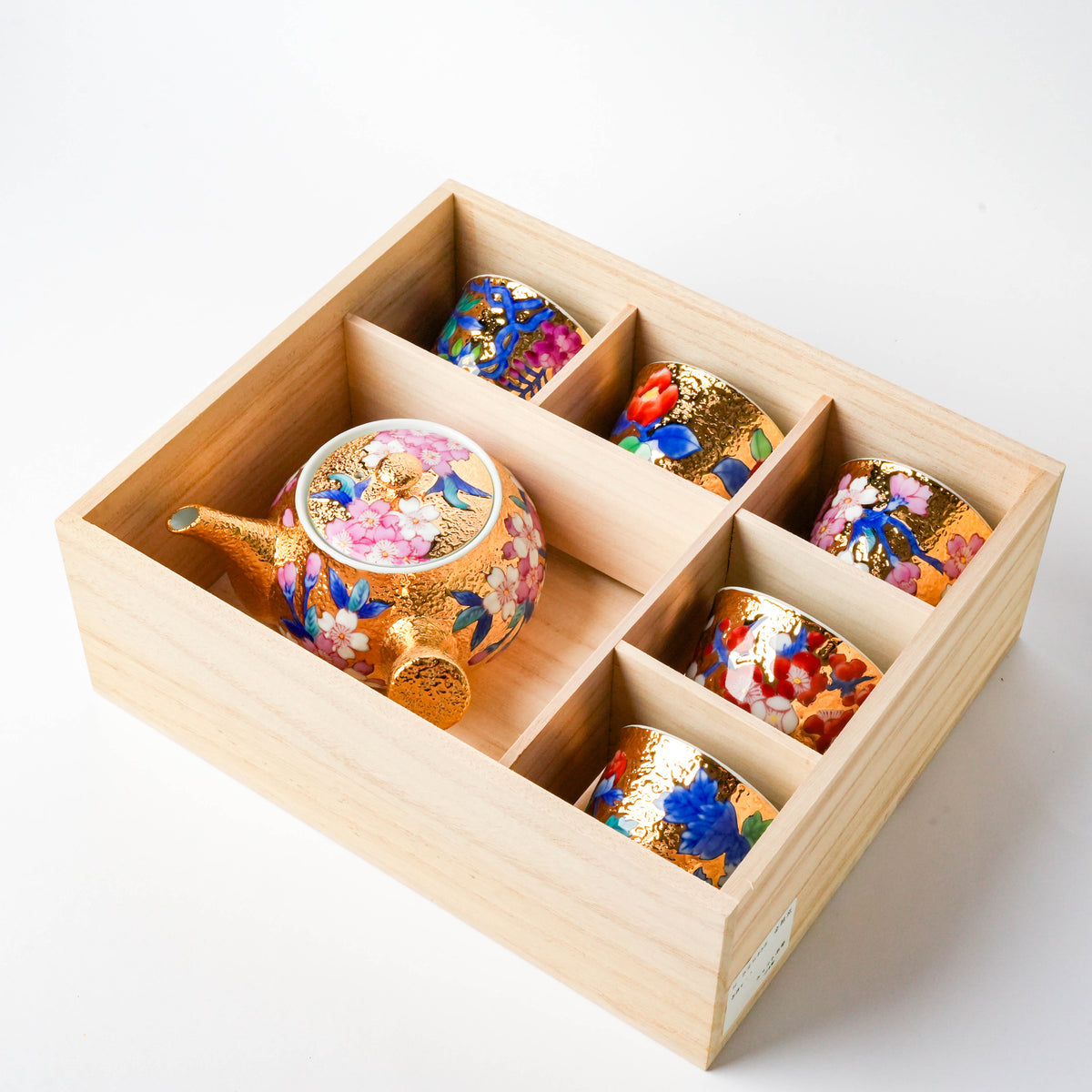 Close-up of the wooden box corner with the decorated ceramic tea set inside, highlighting the detailed floral patterns and gold embellishments