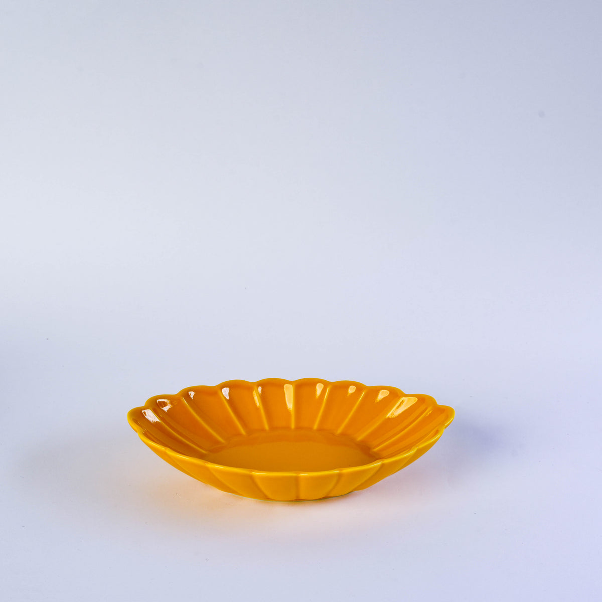 Bright yellow ceramic oval plate with carved floral design, perfect for serving appetizers or desserts on a white background.