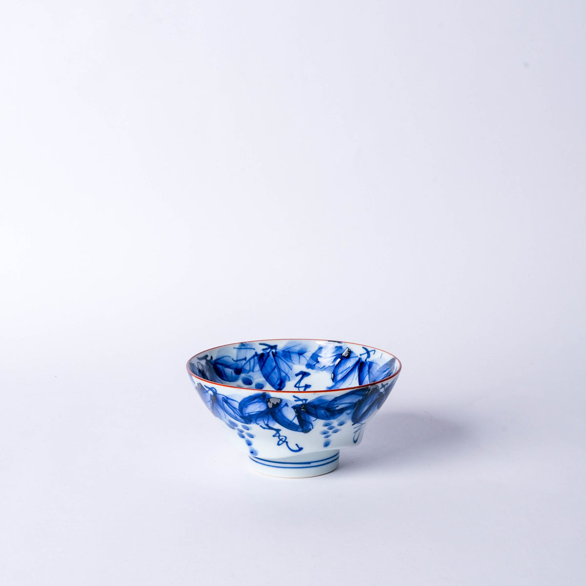 Blue and white Japanese porcelain bowl with intricate brushstroke design, red rim, and floral motifs, used for rice or desserts