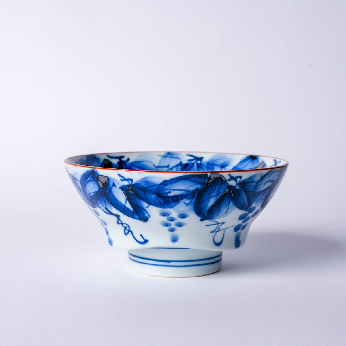 Close-up of the blue and white porcelain bowl with detailed brushwork, floral patterns, and red rim, showcasing traditional Japanese craftsmanship
