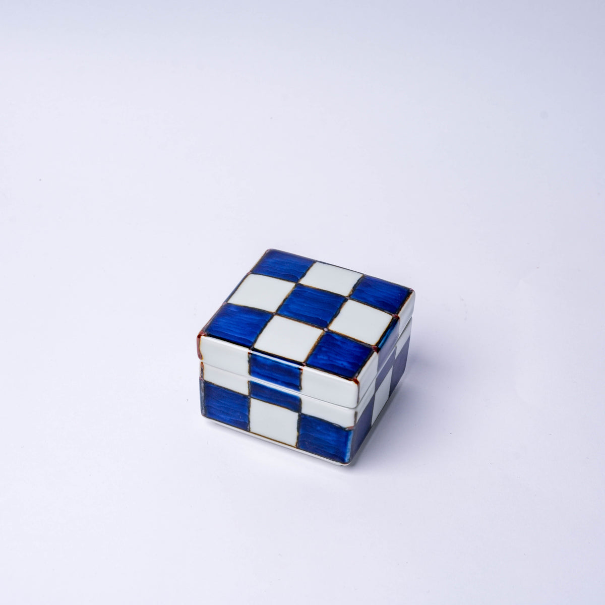 White porcelain checkerboard trinket box with blue and white squares, gold accents, and a removable lid, ideal for small storage