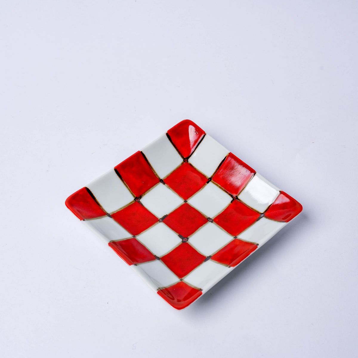 Top view of a Japanese porcelain square plate with red and blue checkered design, used for serving appetizers or desserts