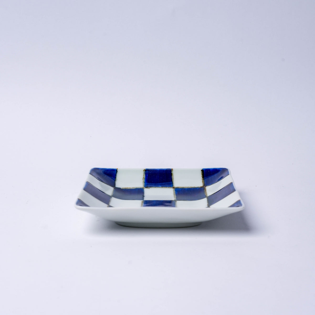 Bottom of a Japanese porcelain square plate with red and blue checkered design, showcasing traditional Japanese craftsmanship