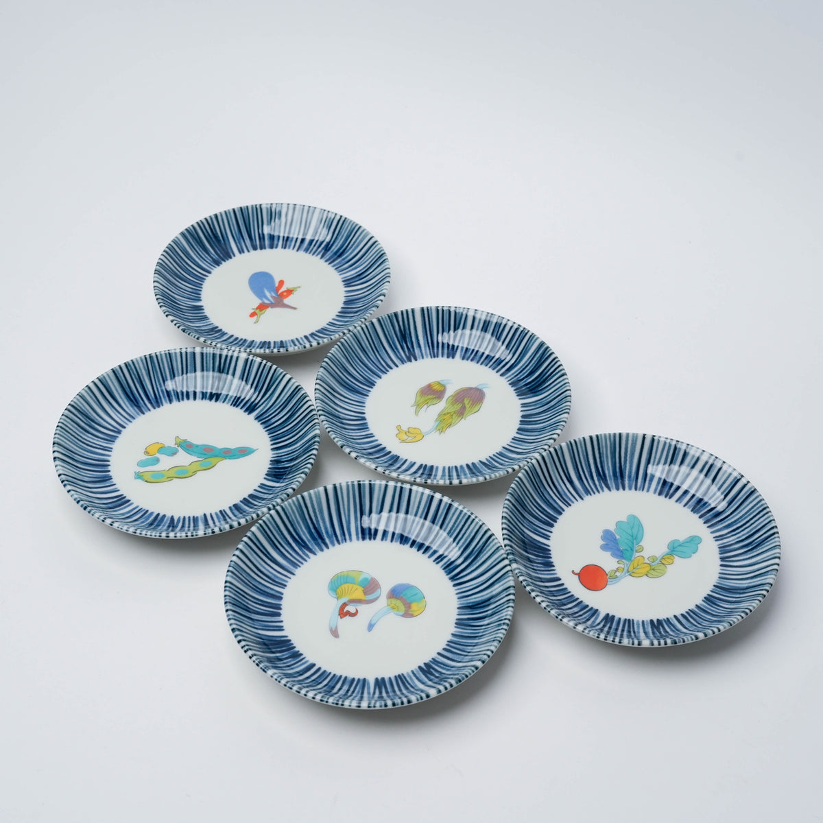 Set of five small porcelain plates with vibrant vegetable motifs and blue striped rims, perfect for serving appetizers or decor.